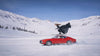 A classic red car driving through the Italian mountainside, with a woman dressed in black skiing