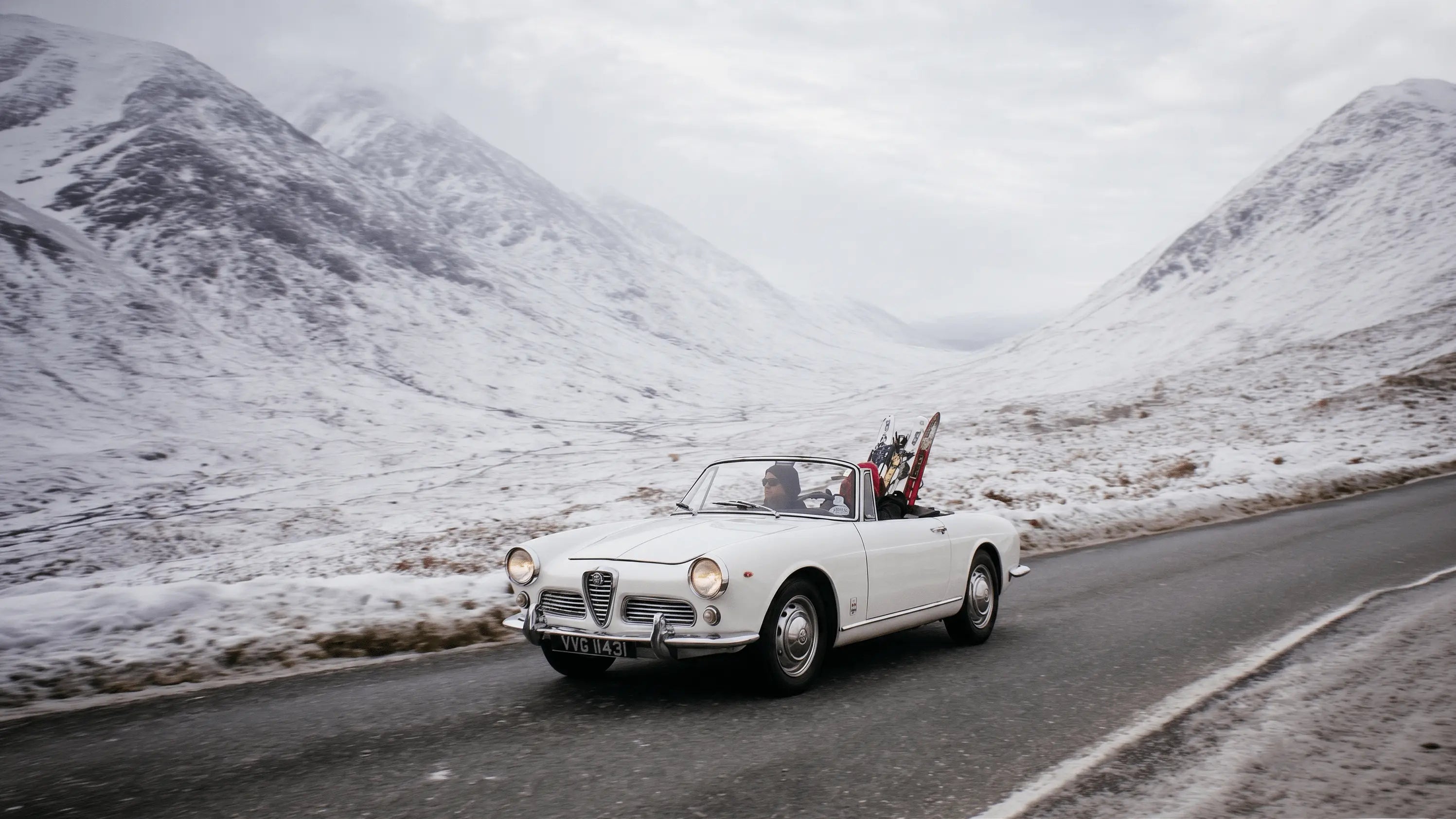 A vintage car driving on a snowy mountain road